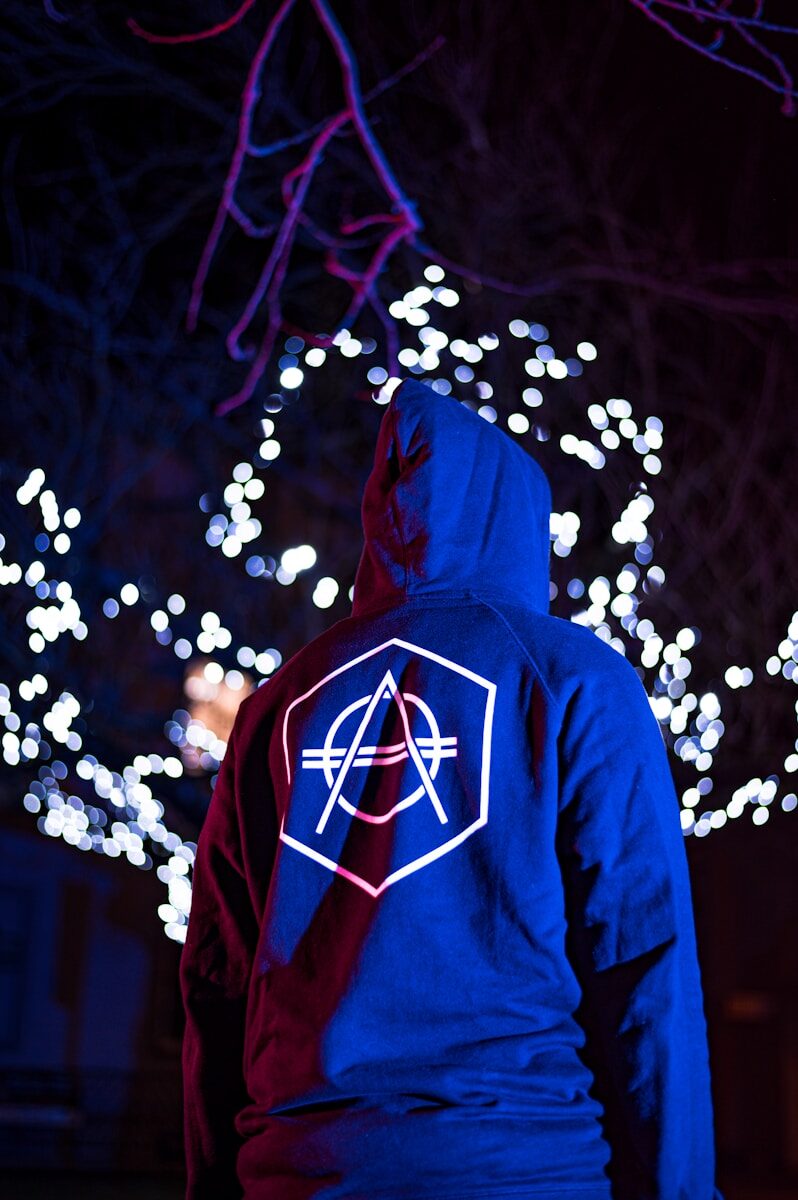 Photo by Jan Kopřiva person in blue and red hoodie standing in front of white string lights